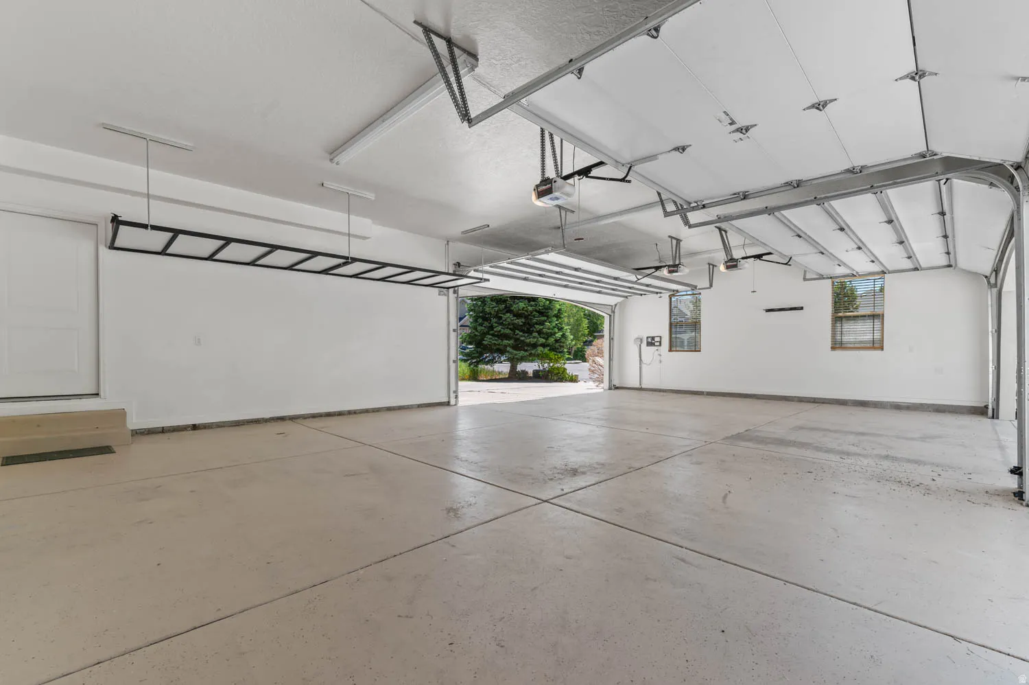 Spacious garage featuring a light-toned concrete floor, white walls, and a white access door