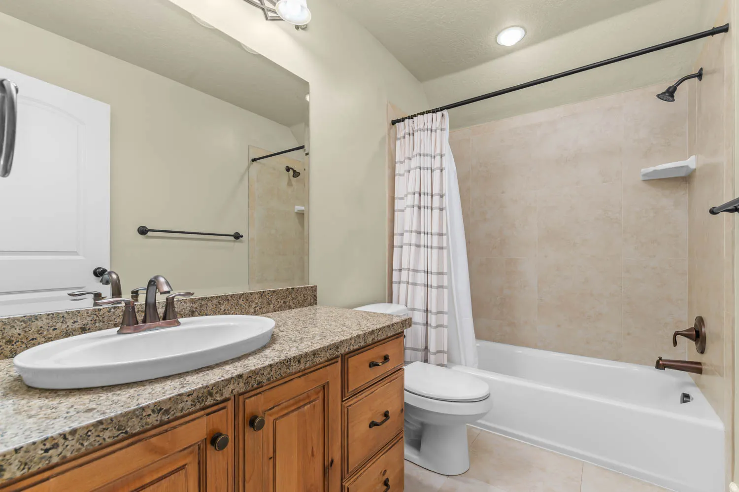 Bathroom featuring a natural wood vanity with a speckled countertop, an oval vessel sink, and an oil-rubbed bronze faucet