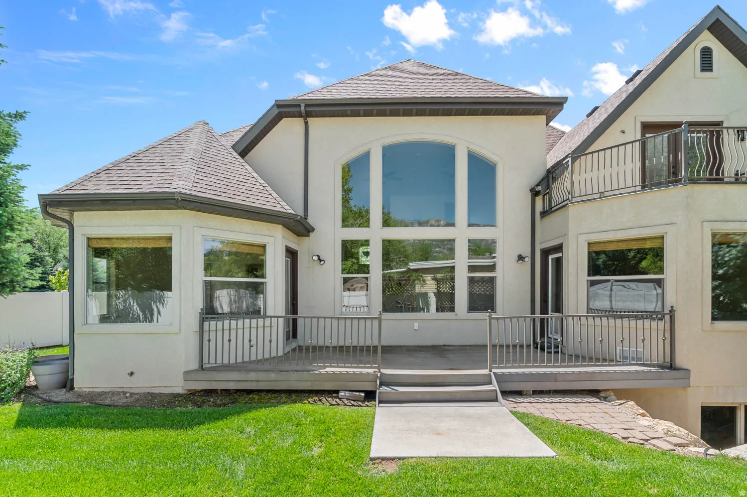 Rear elevation featuring an expansive multi-level deck with metal railings and a substantial arched window
