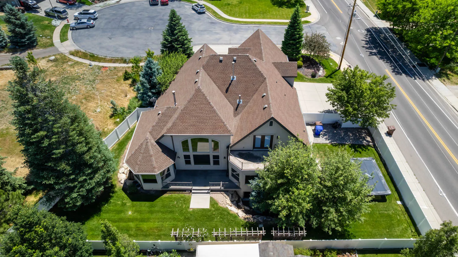 Expansive property featuring a multi-gabled roofline, mature trees, manicured lawns, and a private rear patio with a retaining wall