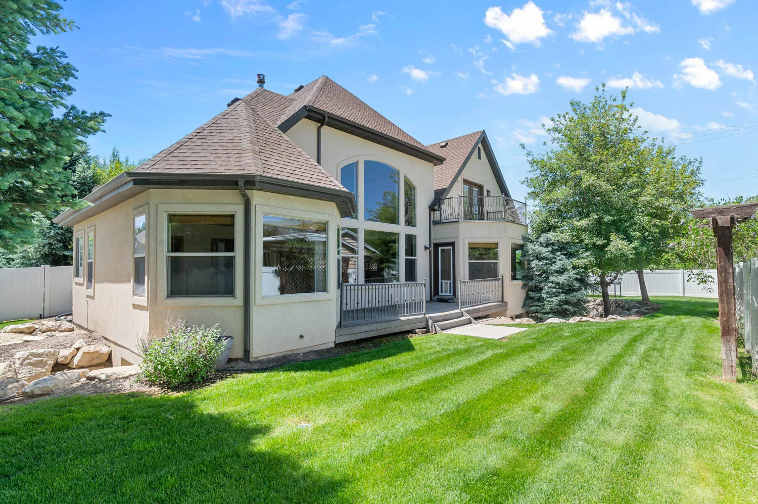 Stucco exterior featuring a multi-level roofline, large picture windows, and a raised deck with metal railings