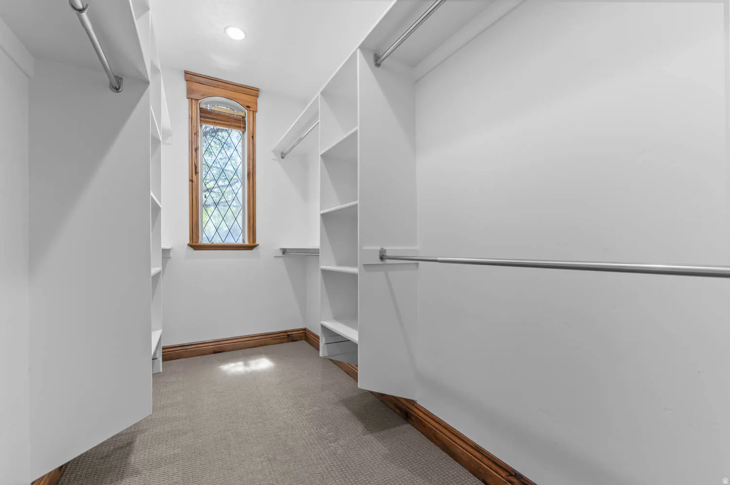 Walk-in closet featuring a decorative window, built-in shelving, chrome hanging rods, recessed lighting, and carpet flooring