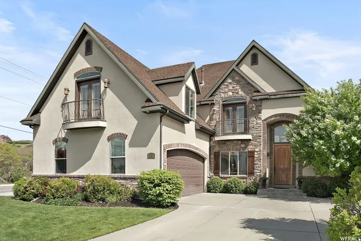 Stucco and stone exterior featuring an arched wood-panel entry door, an arched garage door, decorative iron balconies, and a paved driveway