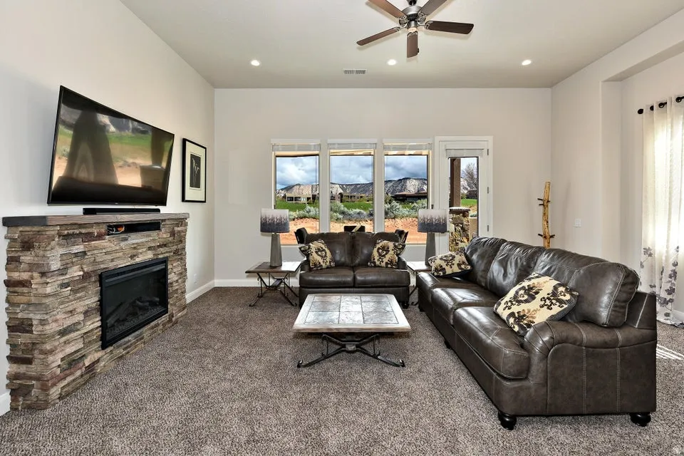 Living area featuring a stone-clad electric fireplace, multiple large windows, a glass-paneled door, and a ceiling fan with integrated lighting