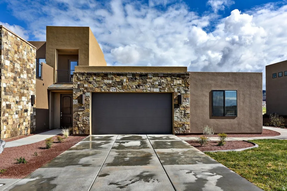 Contemporary stucco exterior featuring stone accents, an integrated garage, a private balcony, and a decorative front door