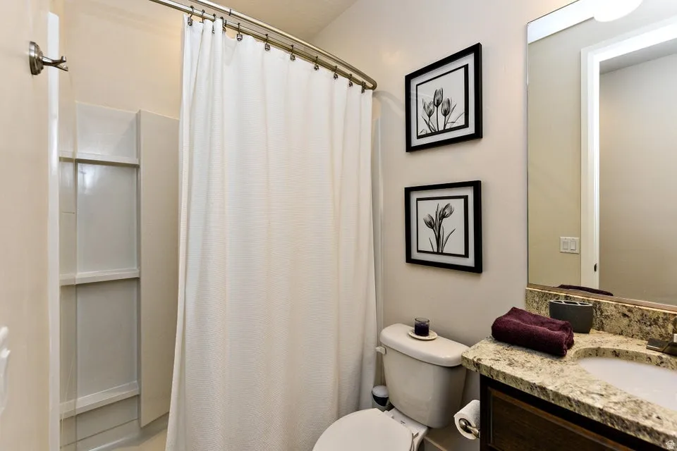 Bathroom featuring a shower-tub combination with a curved shower rod, a vanity with a stone-finish countertop, an integrated sink, and a framed mirror