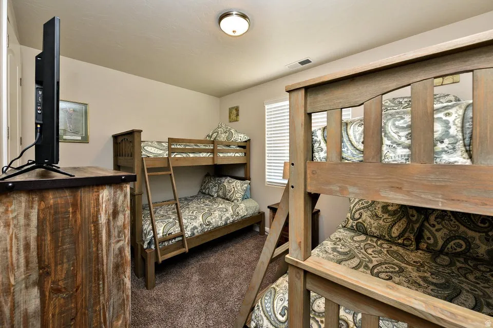 Bedroom featuring two wooden bunk beds, carpet flooring, a ceiling-mounted light fixture, and a built-in window with white blinds