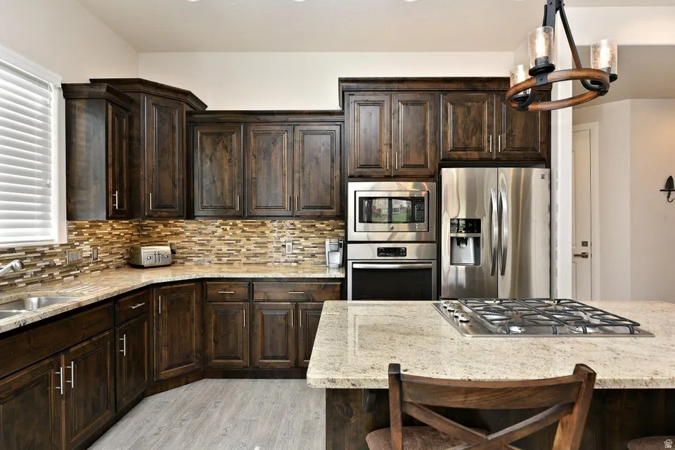 Kitchen featuring dark wood cabinetry, light-toned countertops, stainless steel appliances, and a mosaic tile backsplash