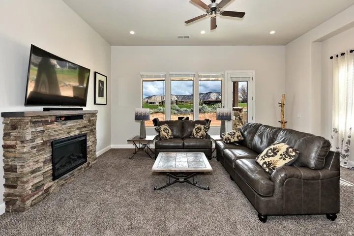 Living area featuring a stone-clad electric fireplace, multiple large windows, a glass-paneled door, and a ceiling fan with integrated lighting