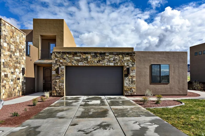 Contemporary stucco exterior featuring stone accents, an integrated garage, a private balcony, and a decorative front door