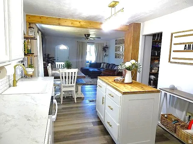 Kitchen featuring white cabinetry, wood-finish flooring, undermount sink with gold-tone faucet, and an island with a wood countertop