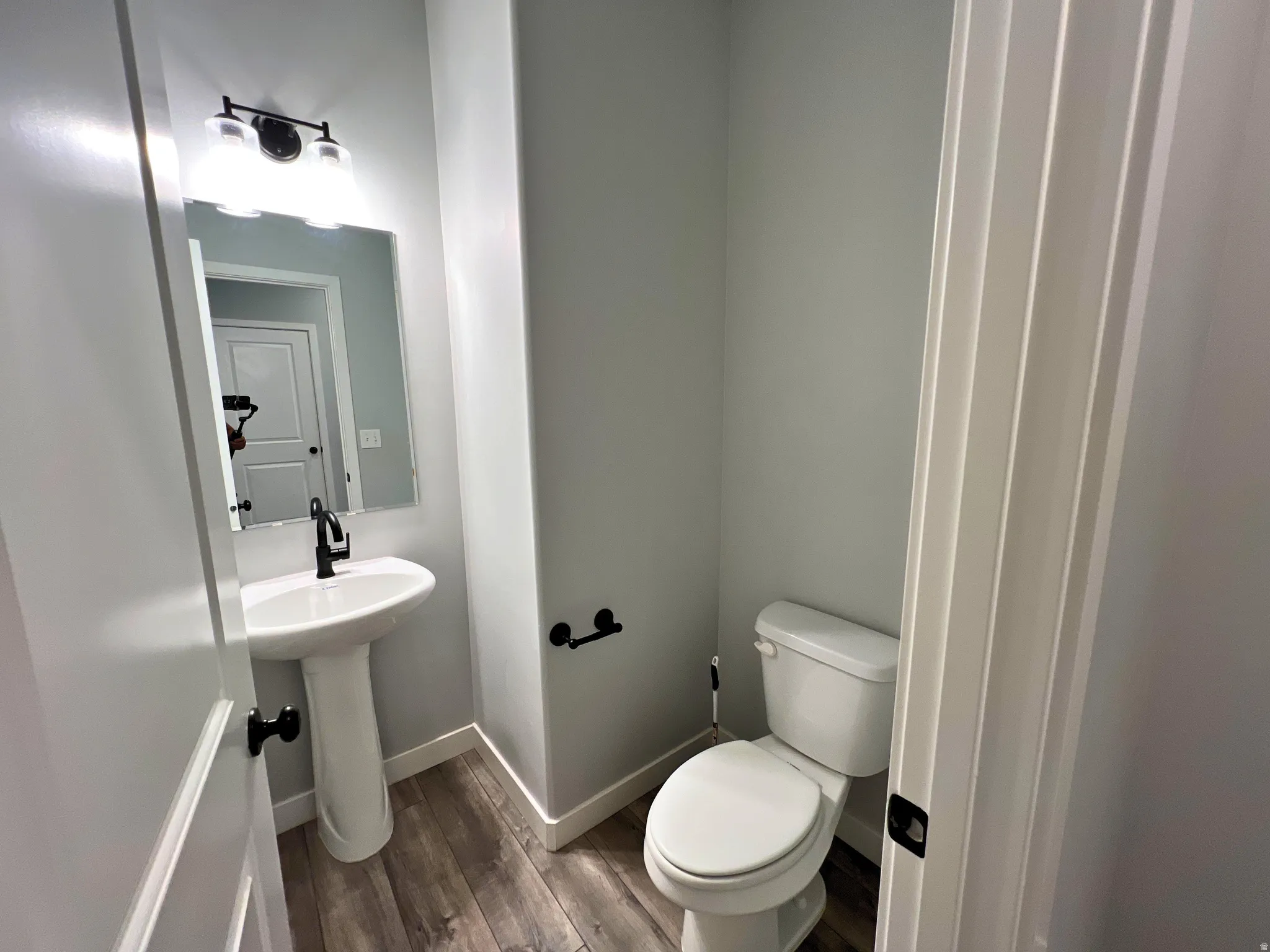 Pedestal sink with a matte black faucet, rectangular wall mirror, and a three-light vanity fixture