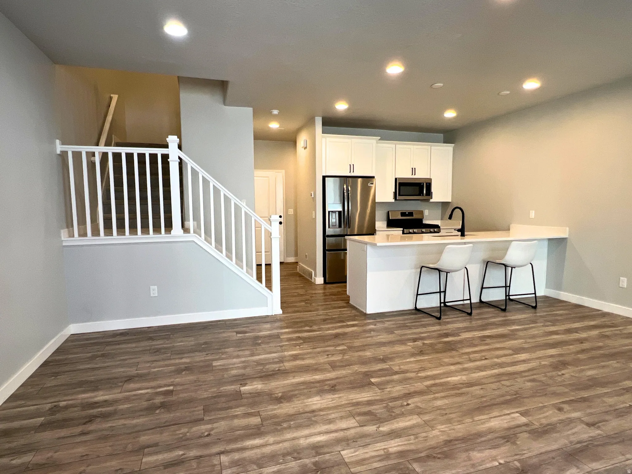 Open-concept living area featuring wood-finish flooring, recessed lighting, and a white baluster staircase