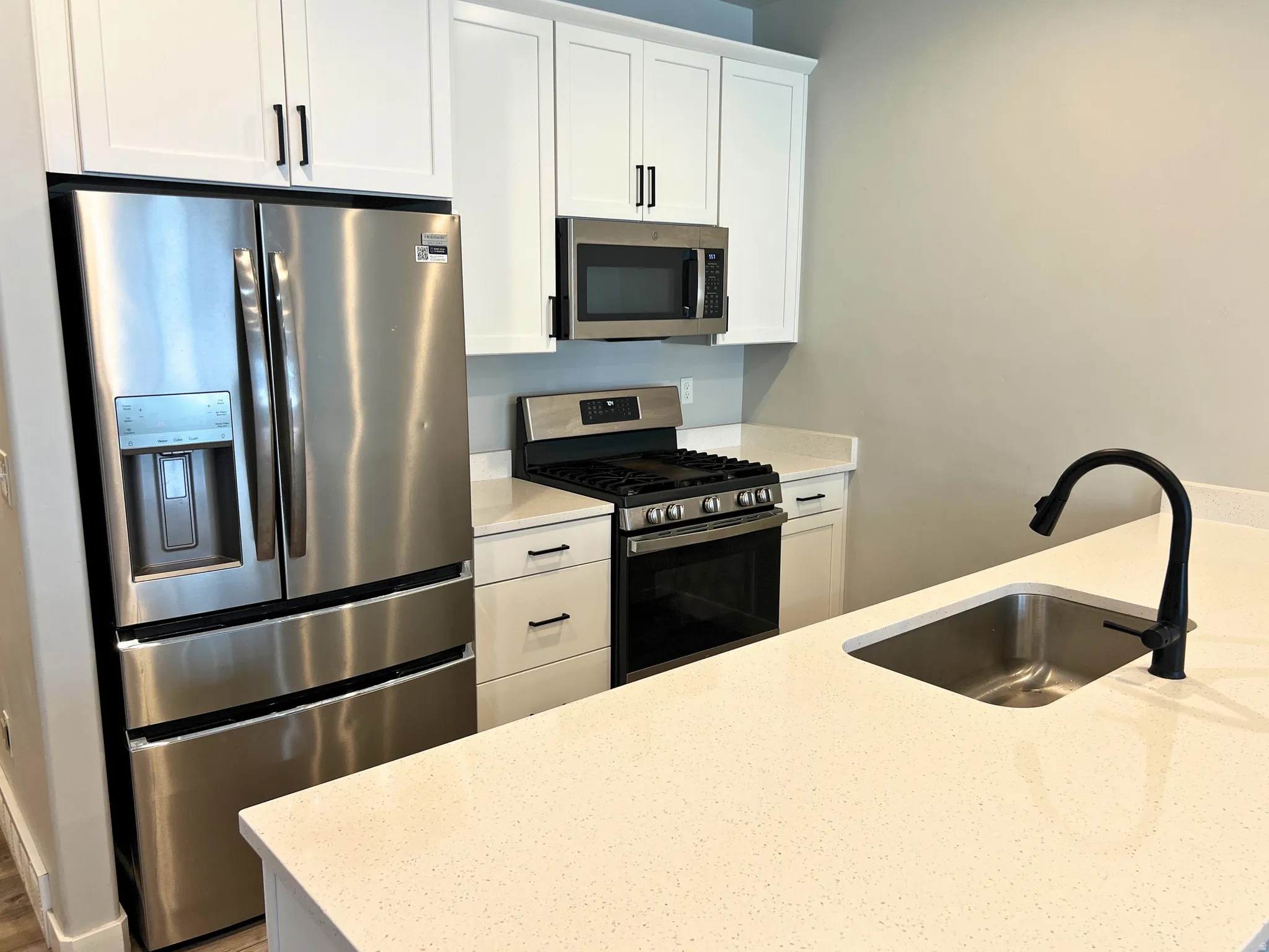 Kitchen featuring stainless steel appliances, white shaker cabinetry, light-toned countertops, a stainless steel undermount sink, and a matte black faucet