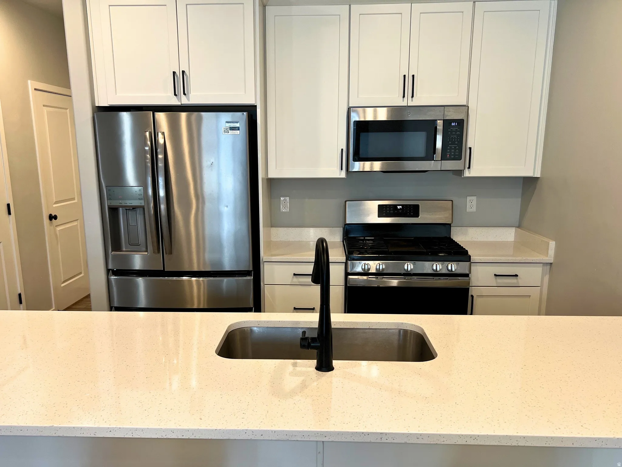 Kitchen featuring white shaker cabinetry, stainless steel appliances, light-toned countertops, and a stainless steel undermount sink with a matte black faucet