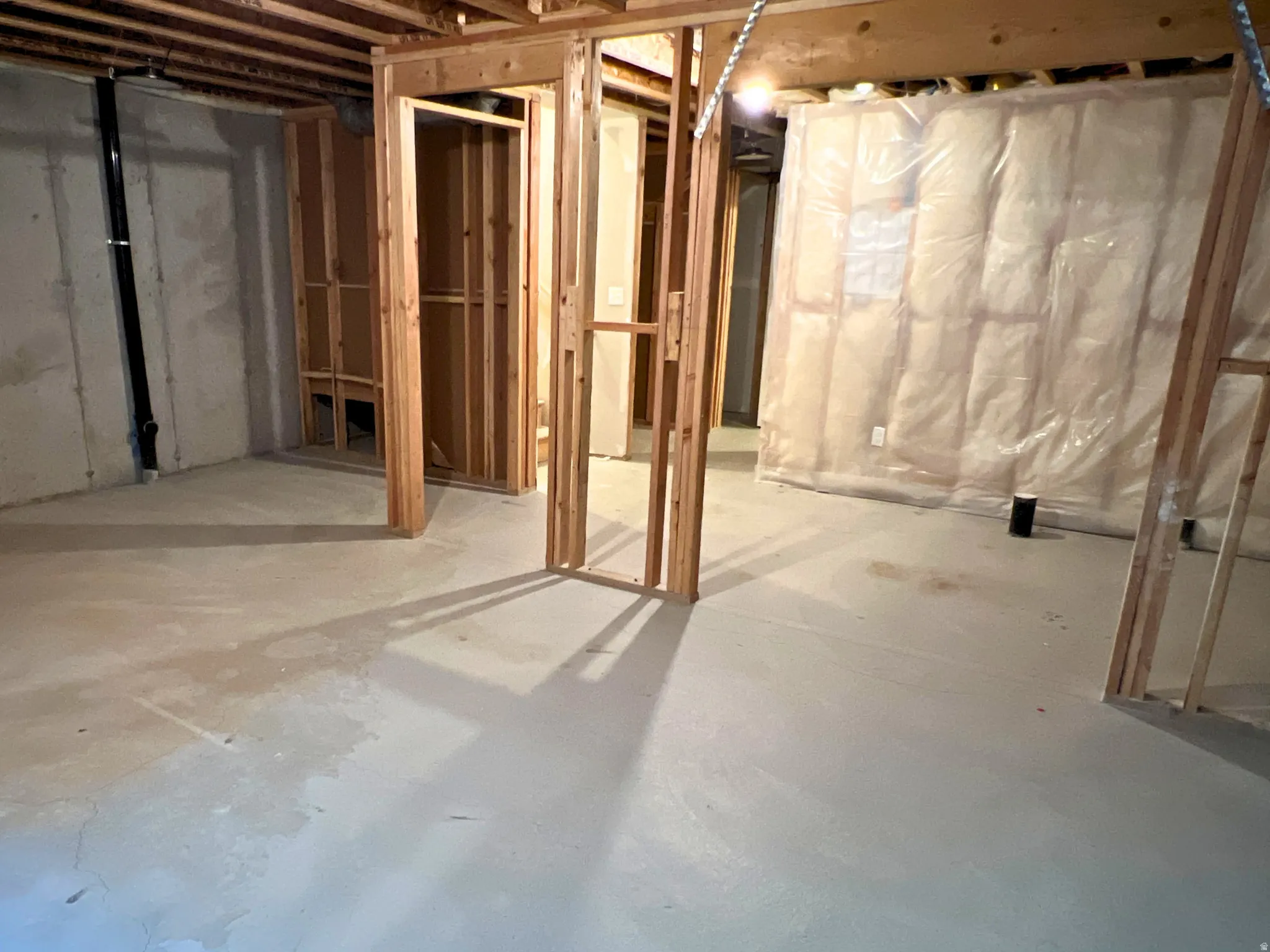 Unfinished basement featuring concrete slab flooring, wood framing for potential rooms, exposed concrete walls, and visible insulation with a plastic vapor barrier