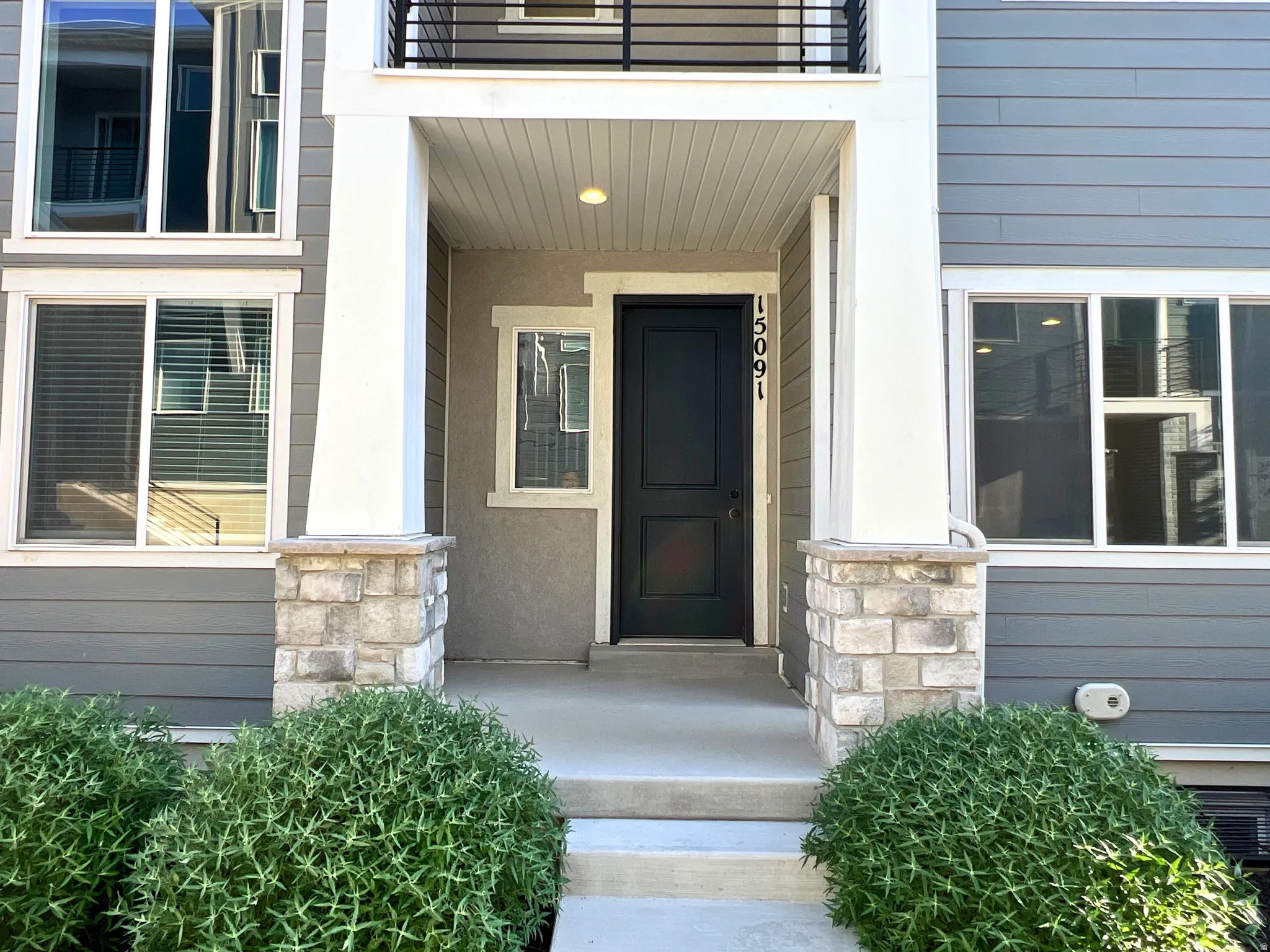 Front entry featuring a dark paneled door with visible house numbers, flanked by large square columns with stone bases