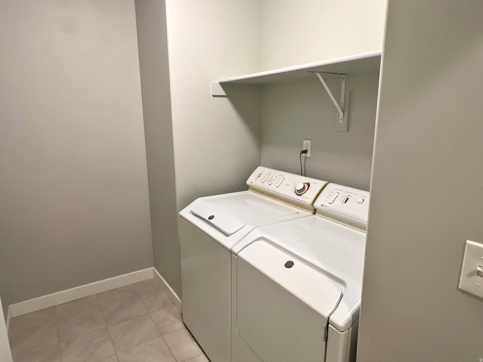 Laundry area with tile flooring, neutral wall tones, and overhead shelving