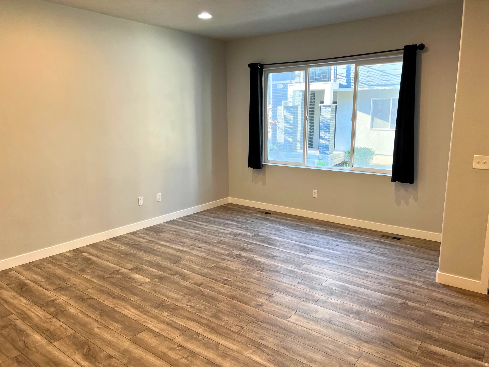 Spacious room featuring wood-finish flooring, neutral wall tones, and white baseboards