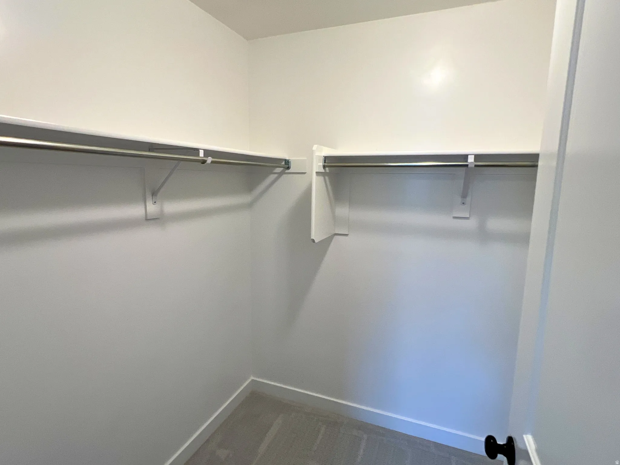 Walk-in closet with ample storage solutions, featuring white walls, white shelving, and chrome hanging rods