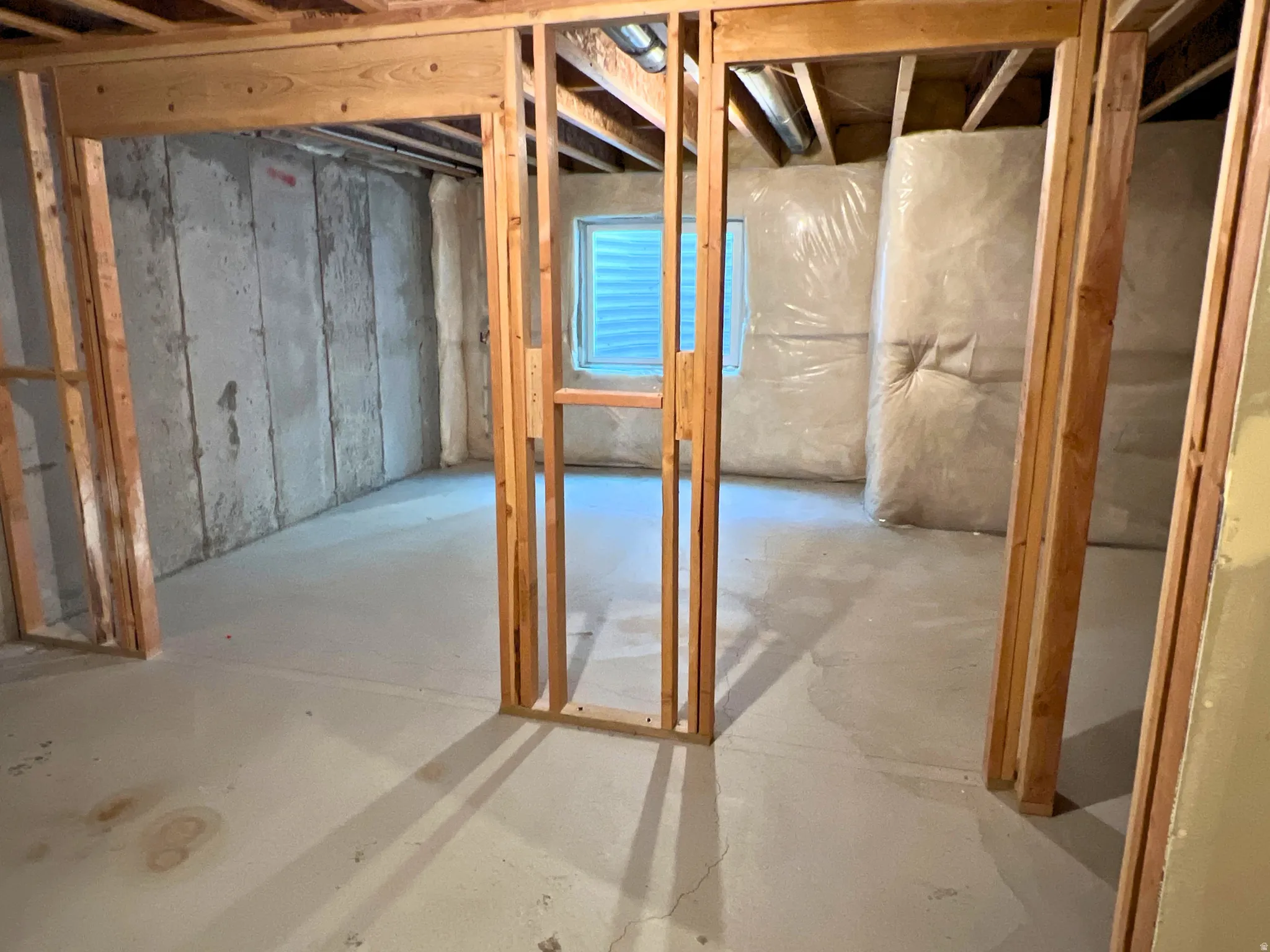 Unfinished basement offering exposed wood framing, concrete flooring, concrete block walls, a visible window, and insulation