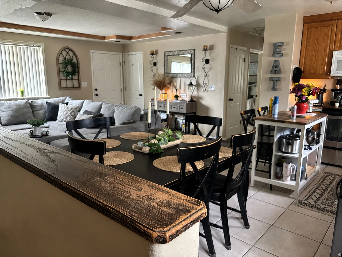 Open-concept living area and dining area with a dark-finish table, a wood-finish half-wall, and a ceiling fan