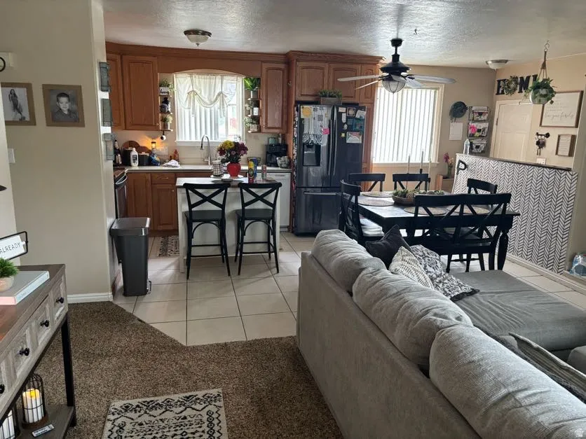 Open concept living area featuring a kitchen with wood cabinetry and an island with bar seating, a dining area with a ceiling fan, and tile flooring throughout the kitchen and dining spaces