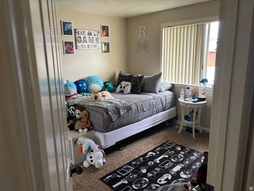 Carpeted bedroom with a single window featuring vertical blinds, light beige walls, and white trim