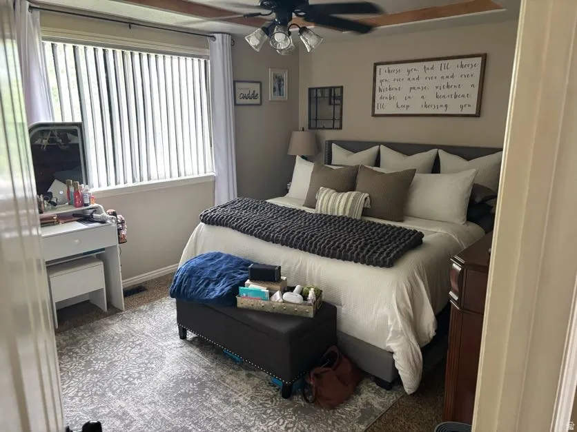 Primary Bedroom featuring a tray ceiling, a ceiling fan with integrated lighting, and a large window with vertical blinds