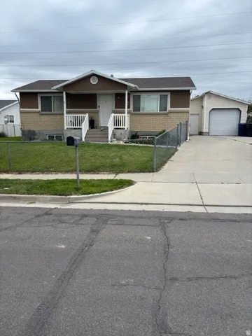 Rambler residence featuring a covered front porch with white railings, a front lawn fully fencing, a detached garage with an automatic door, and a concrete driveway