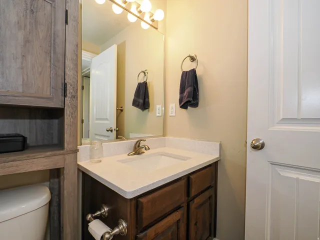 Bathroom vanity featuring a light-toned countertop with integrated sink, dark wood-finish cabinetry, and a brass-toned faucet
