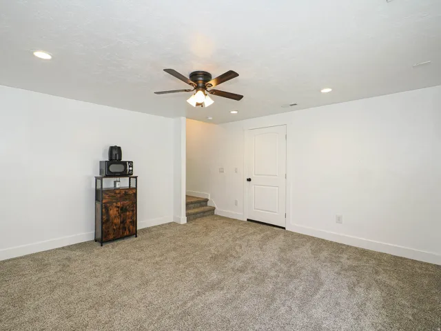 Spacious carpeted room featuring recessed lighting, a ceiling fan with light fixture, and a white paneled door