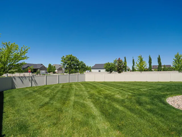 Expansive backyard featuring a manicured lawn with striped patterns, a section of decorative rock landscaping, and mature trees