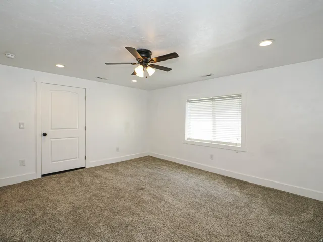 Carpeted room featuring a ceiling fan with integrated lighting, recessed lighting, a two-panel interior door with matte black hardware, and a window with blinds