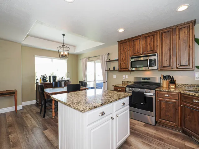 Kitchen featuring granite countertops, wood-finish flooring, stainless steel appliances, and a tray ceiling with recessed lighting