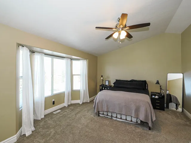 Carpeted room featuring a bay window with blinds, a ceiling fan with integrated lighting, and vaulted ceilings