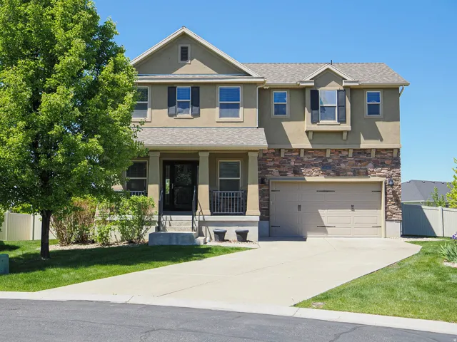 Two-story stucco and stone-front residence featuring a covered entry porch with iron railings, a two-car garage with a panel door, and a concrete driveway