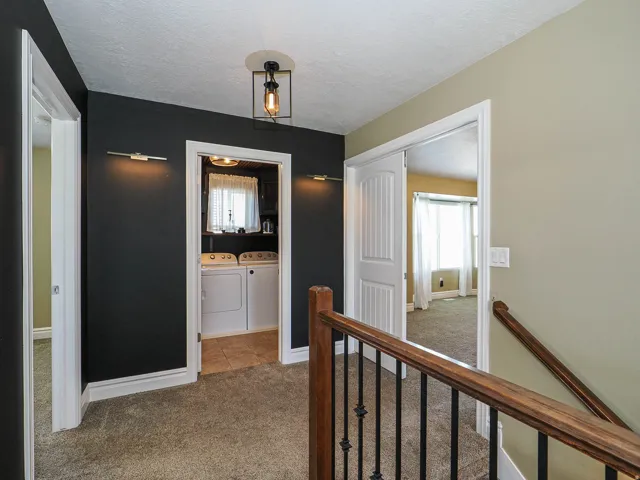 Upper-level hallway with carpet flooring, a contemporary ceiling light fixture, and a laundry area featuring a tile floor and built-in cabinetry