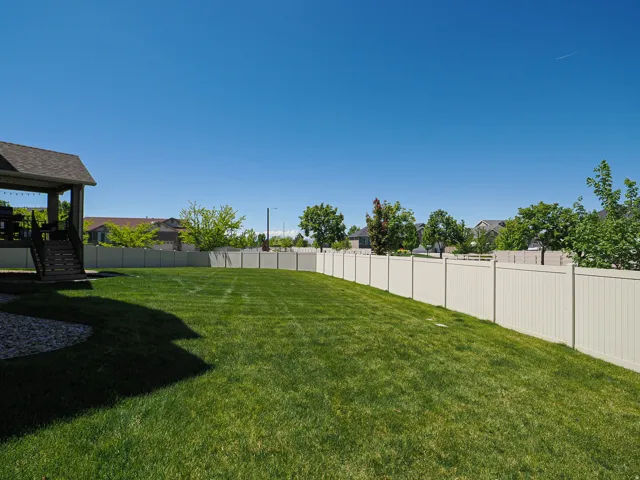 Expansive backyard featuring a large green lawn, full privacy fencing, and a covered patio structure with stairs