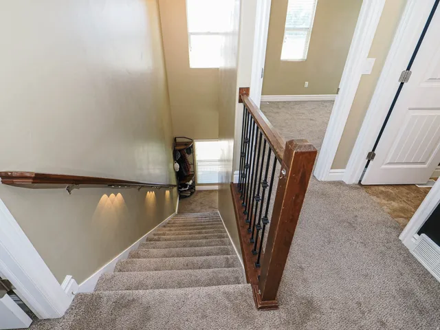 Carpeted staircase with dark wood newel post and wrought iron balusters