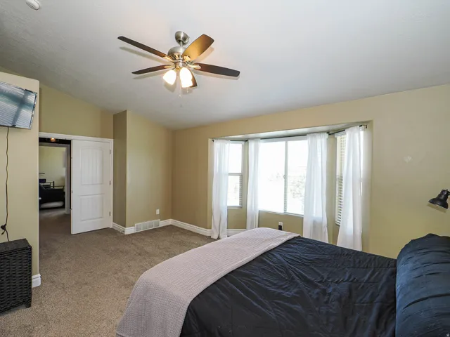Room with bay window, carpeted flooring, a ceiling fan with integrated lighting, and painted walls
