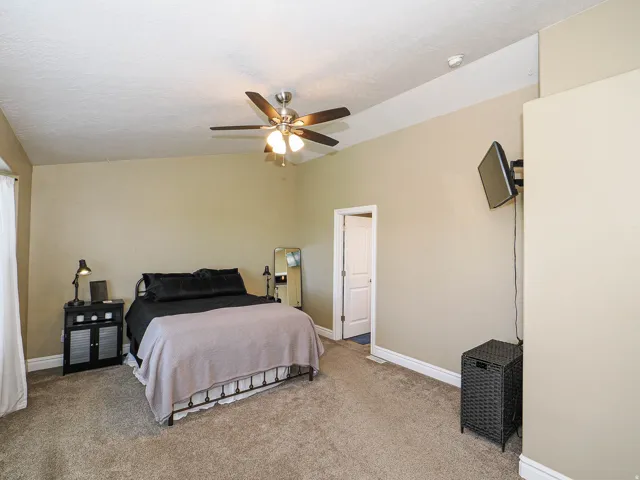 Carpeted room featuring a ceiling fan with integrated lighting, a wall-mounted television bracket, and a white six-panel interior door