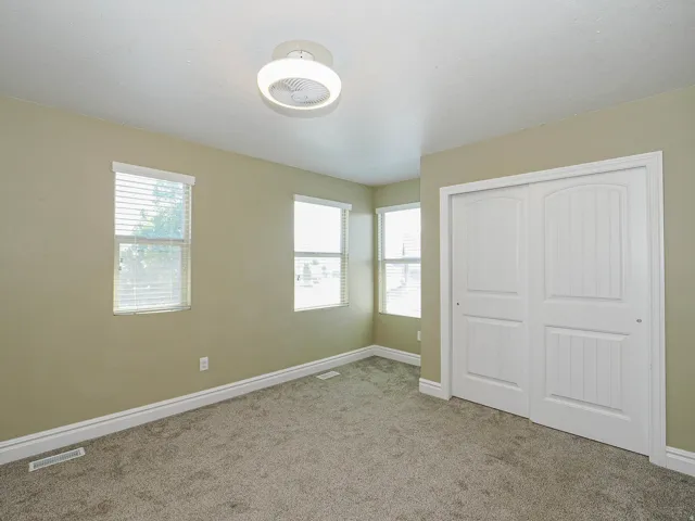 Carpeted room featuring three windows with blinds, a ceiling-mounted light fixture, and a bi-fold closet with panel doors