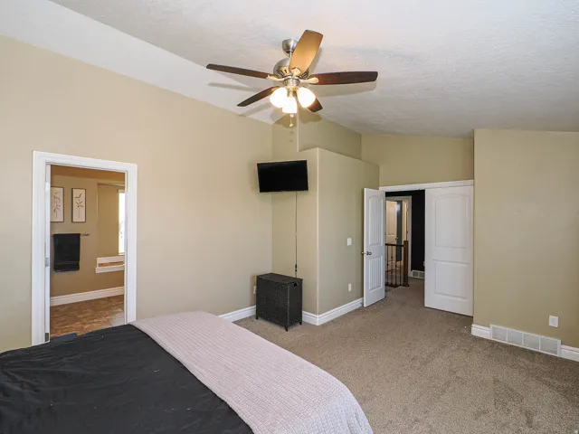 Carpeted room featuring a ceiling fan with integrated lighting, a wall-mounted television, and two entryways with white doors