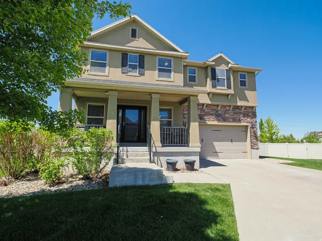 Stucco exterior featuring a covered porch with column supports, stone facade accents, a two-car garage, and a concrete driveway