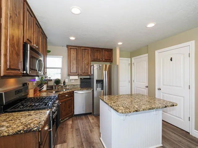 Kitchen featuring wood cabinetry, stainless steel appliances, speckled countertops, a central island with beadboard paneling, and wood-finish flooring