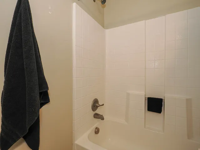 Bathtub with a shower combination featuring white tiled walls, a built-in soap dish, and bronze-finish fixtures