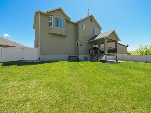 Expansive rear lawn featuring a covered deck with stairs, a privacy fence, and a bay window
