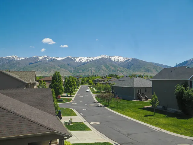 Streetscape with residential properties, manicured lawns, and mature trees, set against a backdrop of snow-capped mountains