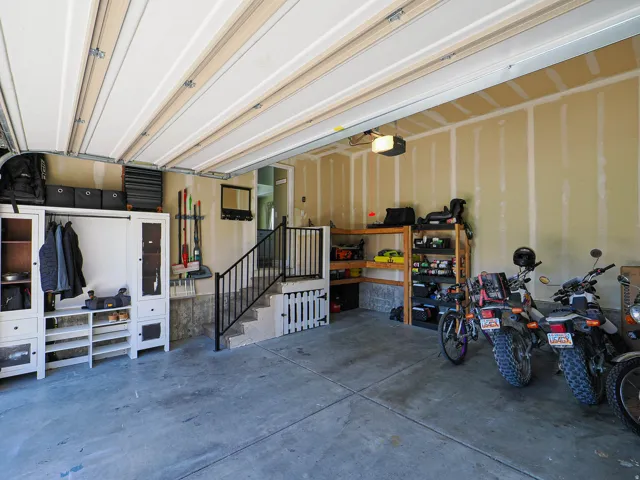 Spacious garage featuring a concrete floor, exposed ceiling joists, an automatic garage door opener, and a built-in staircase with a black metal railing